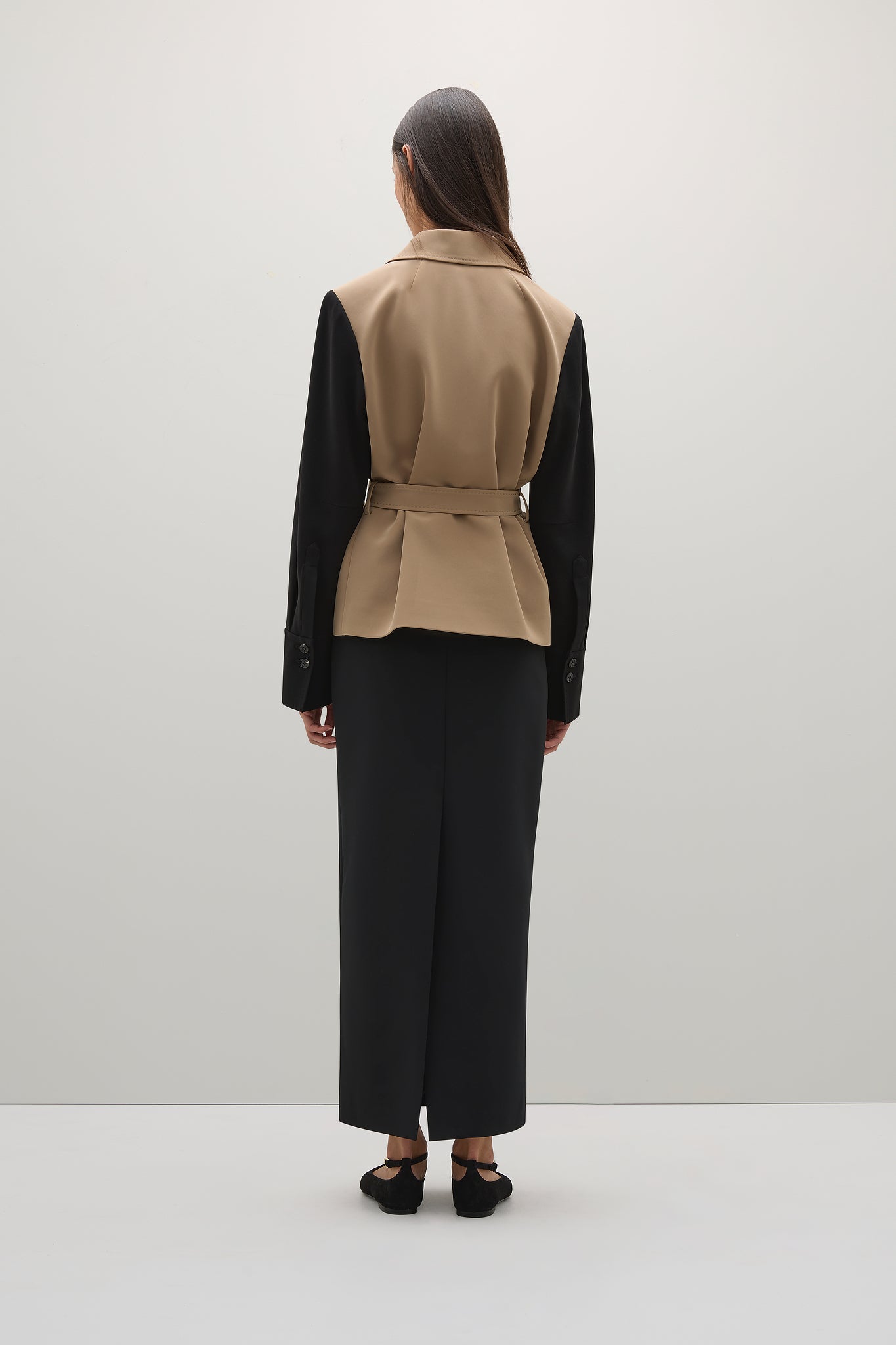 Person wearing a beige vest over a black shirt with wide-leg pants on a white background