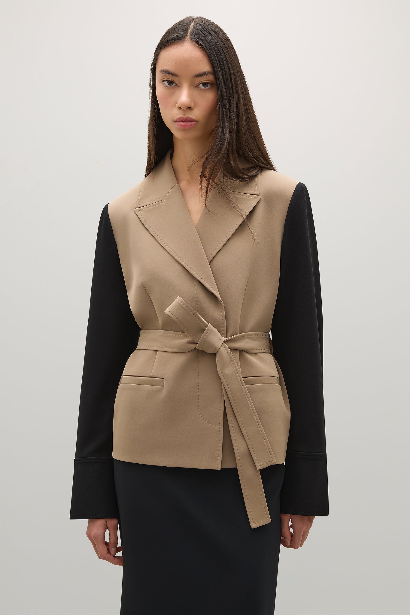 Woman wearing a beige vest over a black outfit on a white background