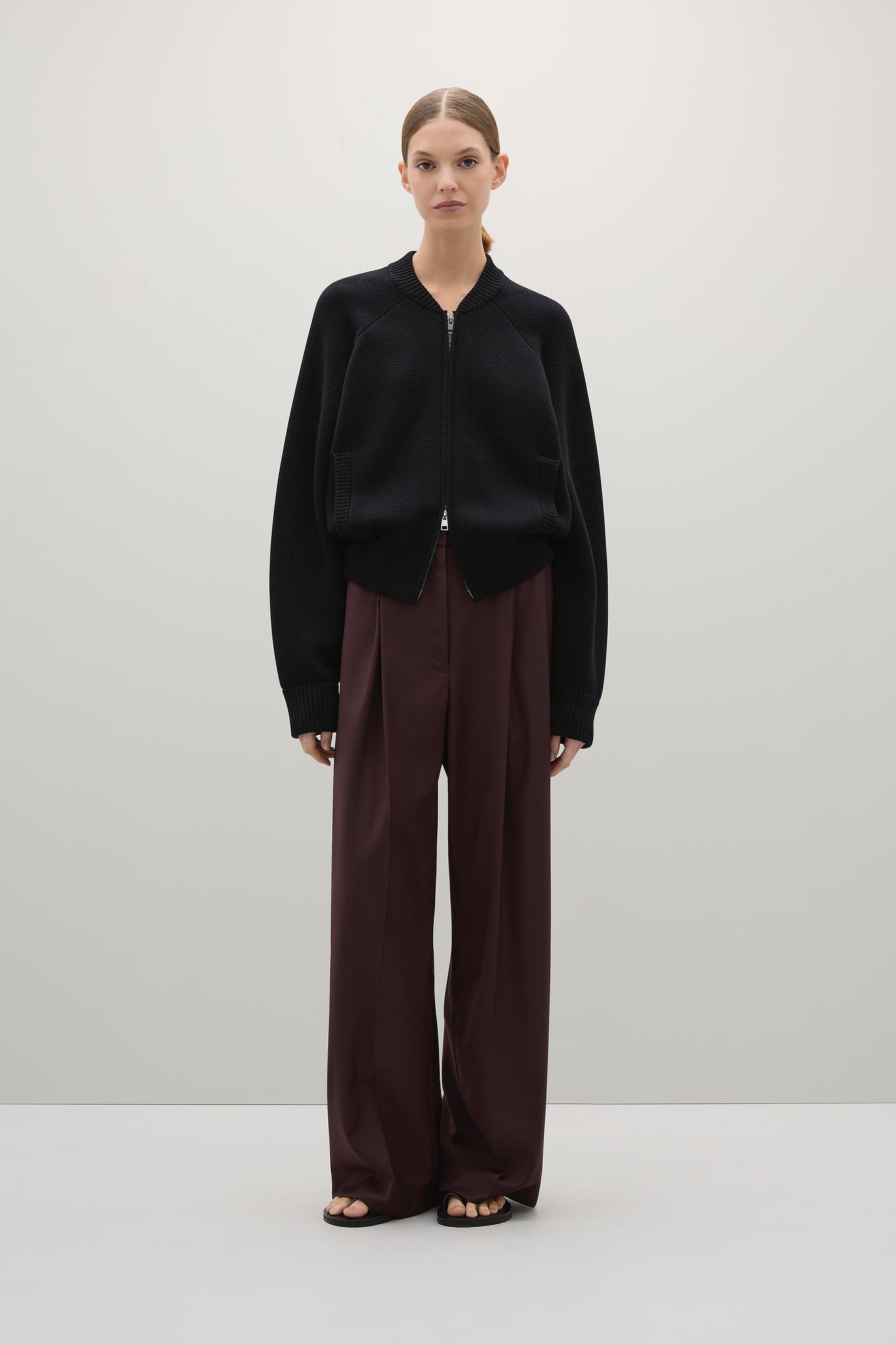 Model wearing a black oversized sweater and brown pants on a white background