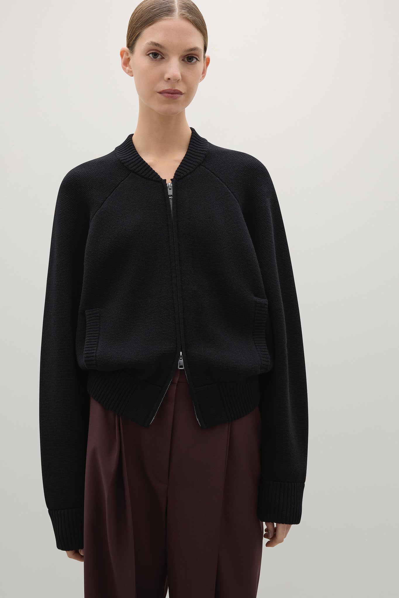 Person wearing a black zip-up sweater over a burgundy outfit on a light gray background