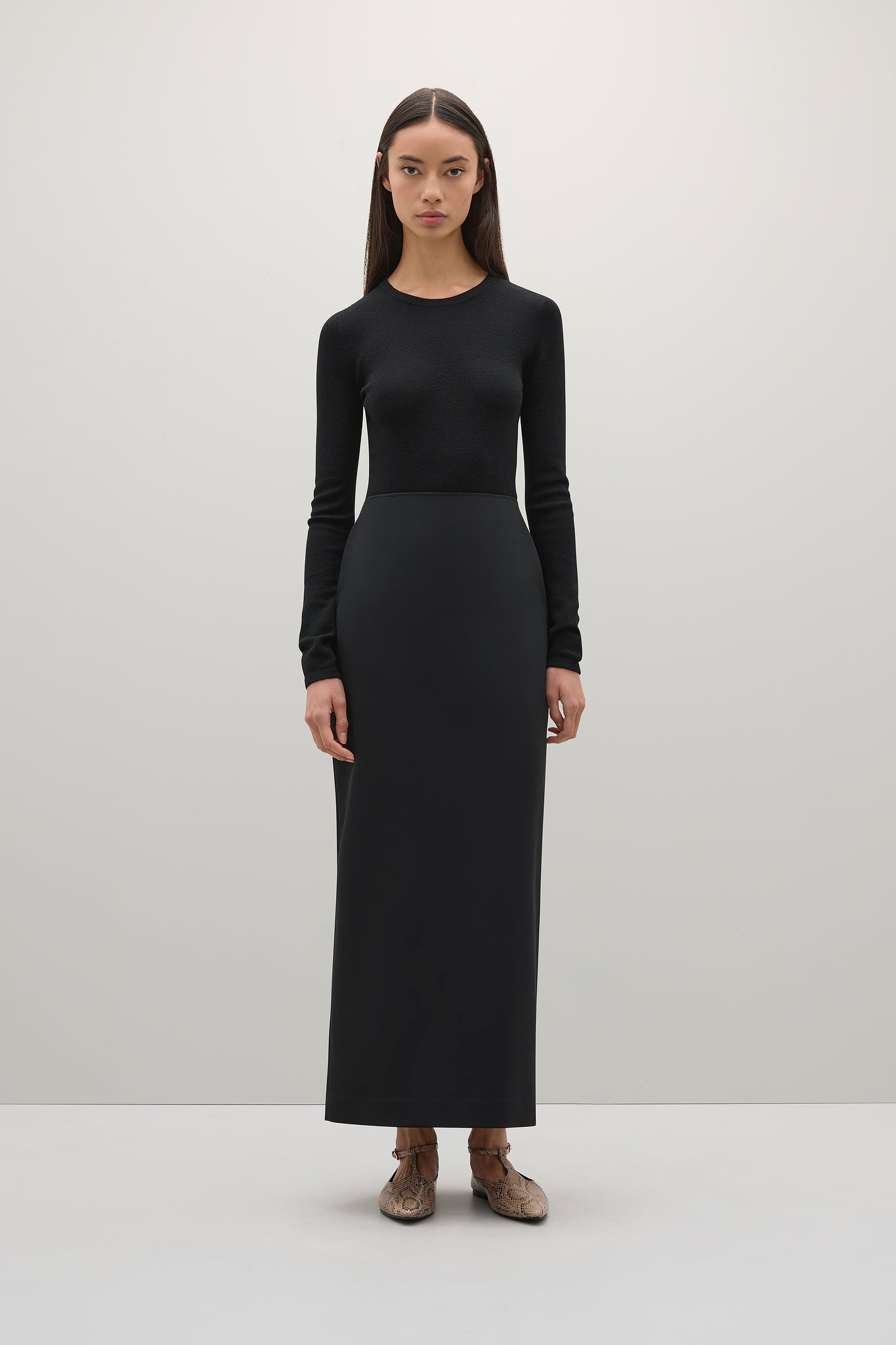 Person wearing a black long-sleeve top and black skirt on a white background
