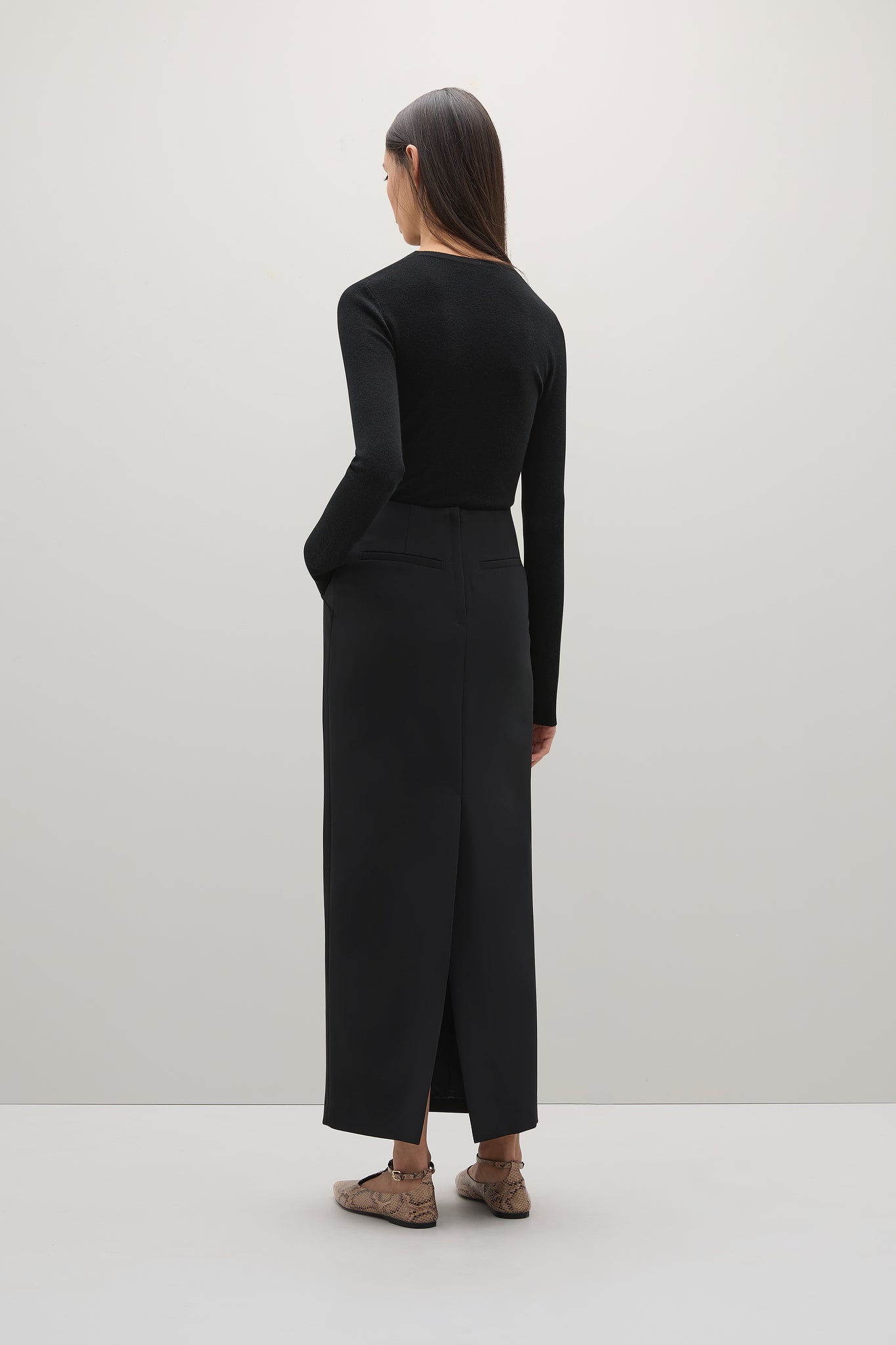 Person wearing a black long-sleeve top and black skirt on a white background