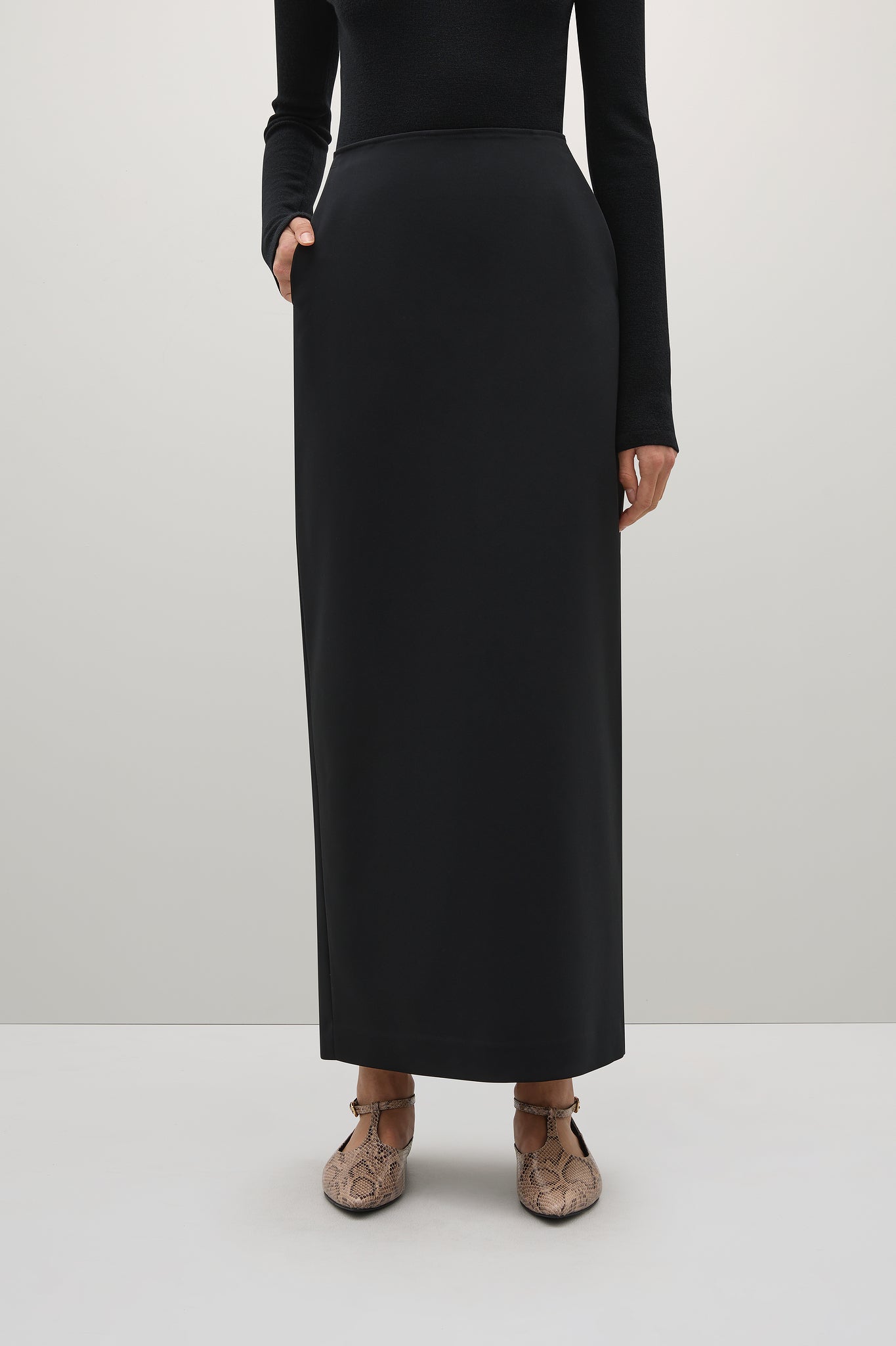 Person wearing a black long-sleeve top and black skirt on a white background