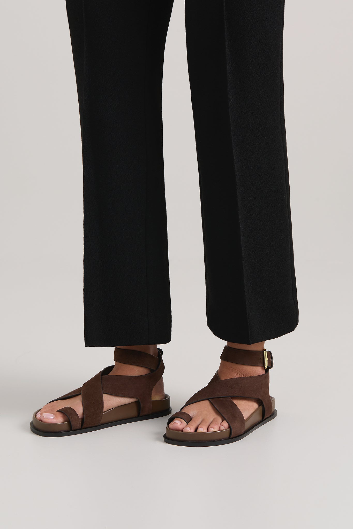 Brown sandals worn with black pants on a plain background