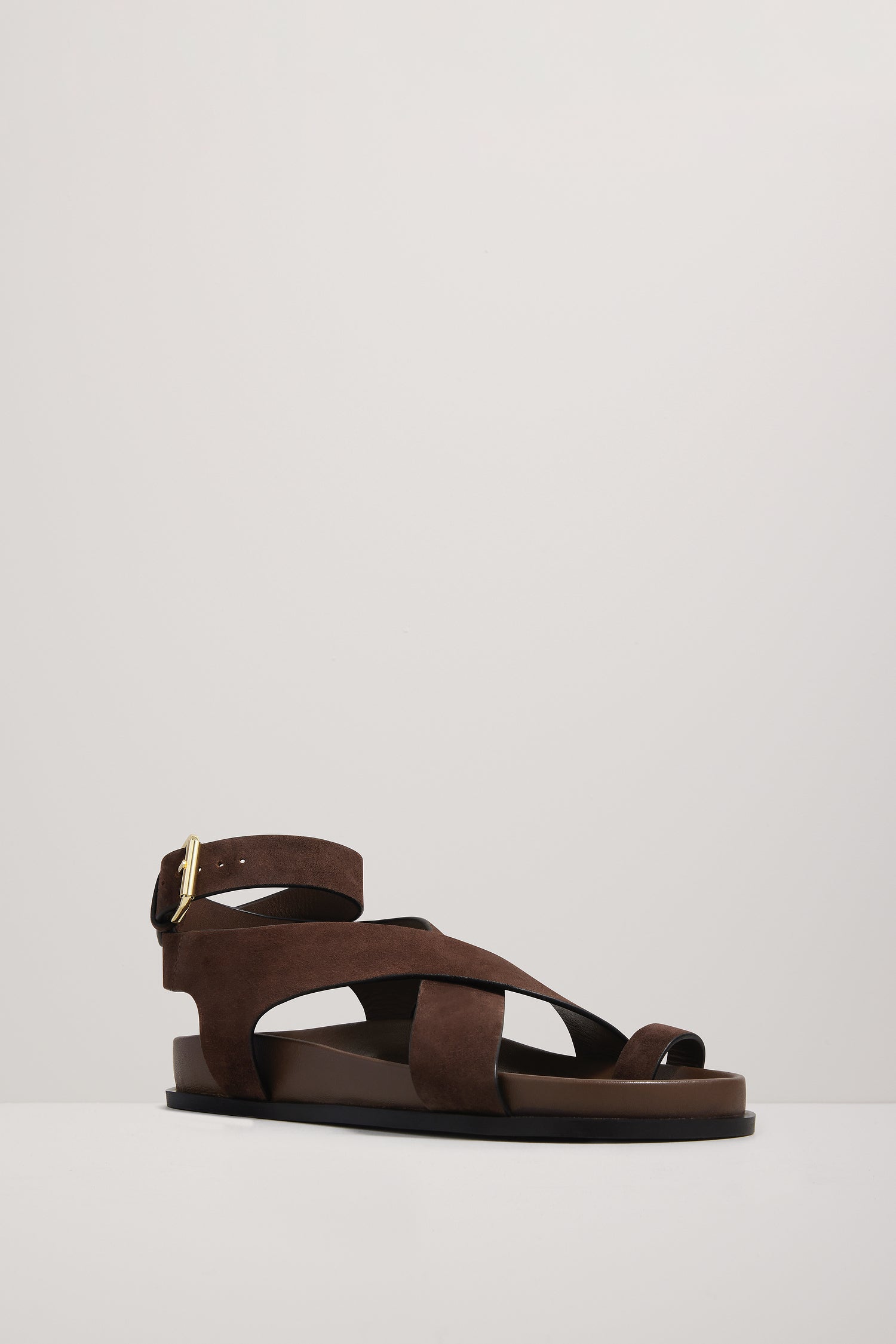 Brown sandal with criss-cross straps on a light gray background
