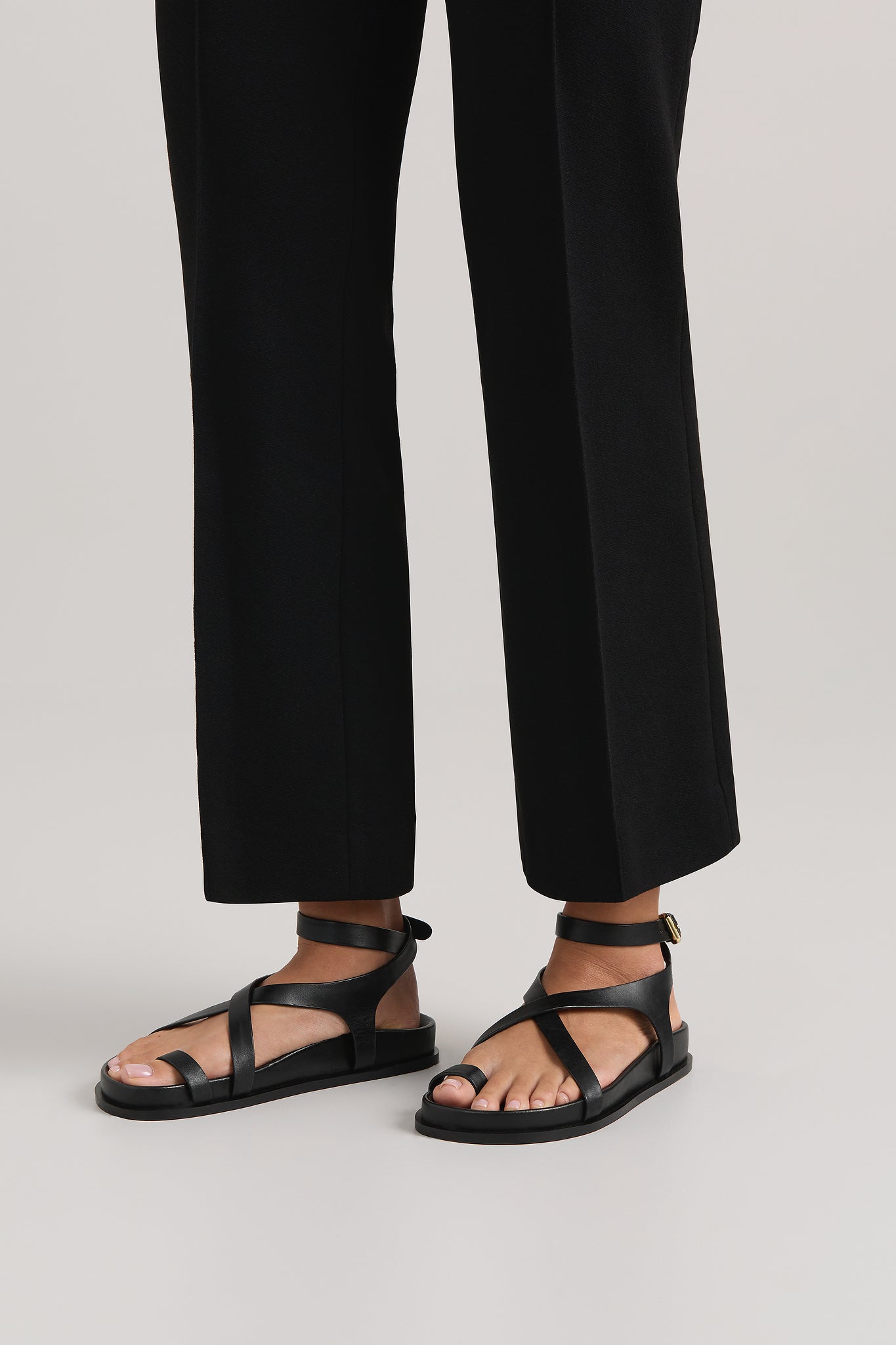Black sandals worn with black pants on a light gray background