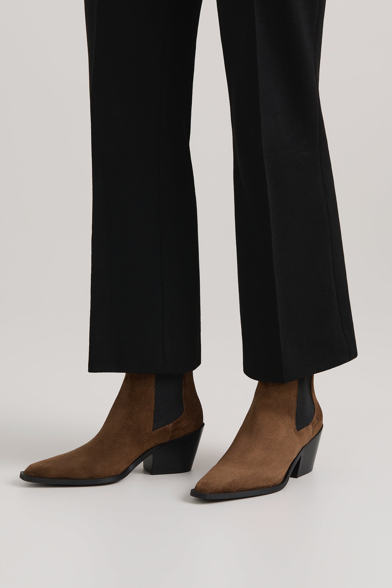 Brown suede boots worn with black pants on a white background