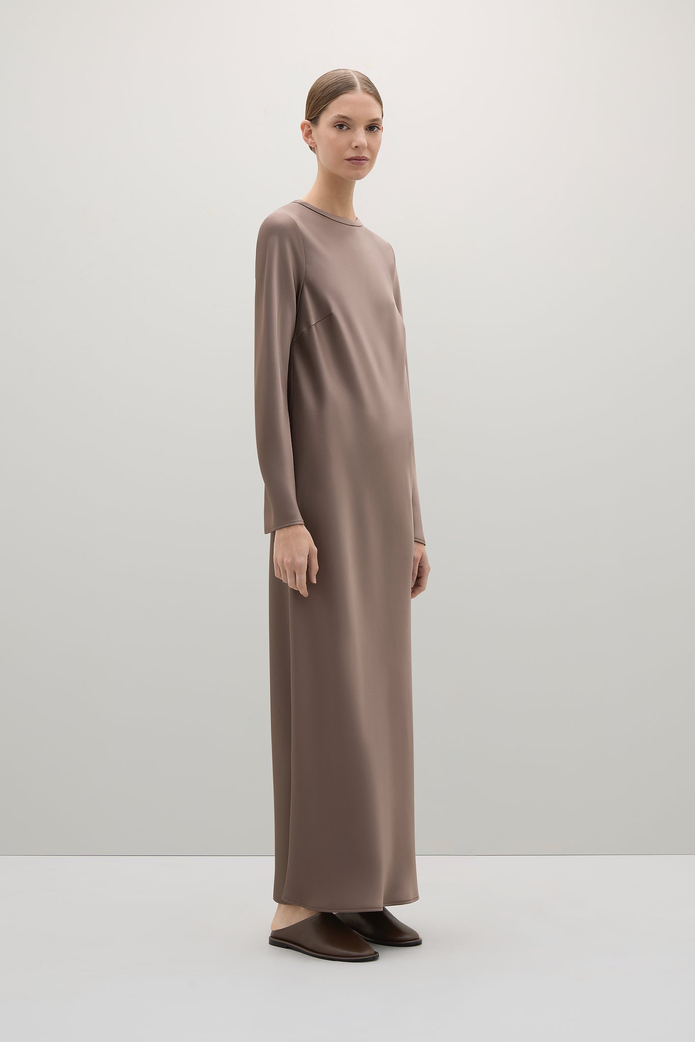Woman wearing a long brown dress against a white background
