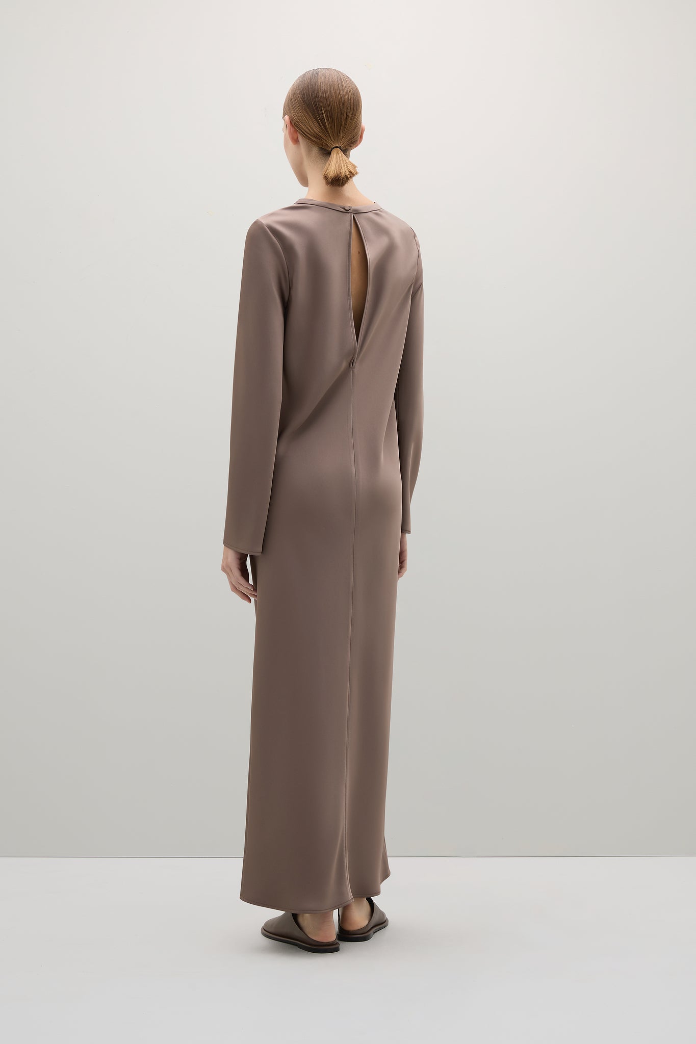 Woman wearing a long brown dress with a cutout back on a white background