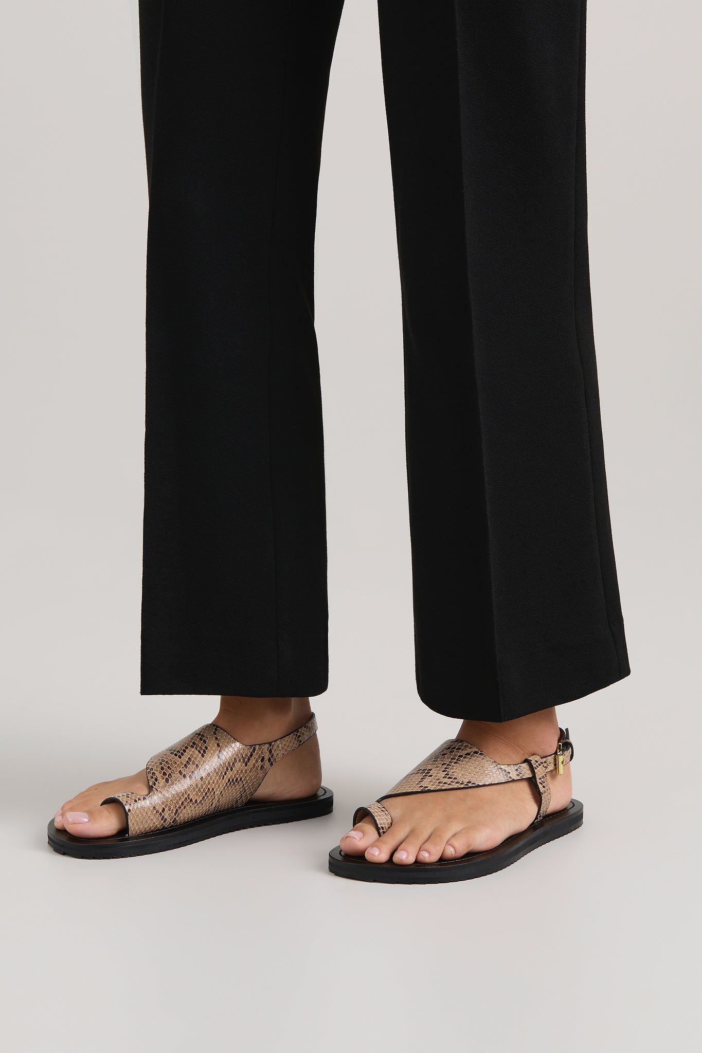 Person wearing black sandals with snake print on a plain background