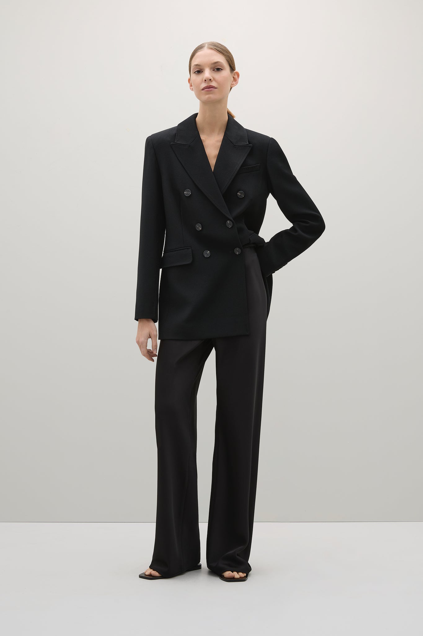 Woman wearing a black suit standing against a white background