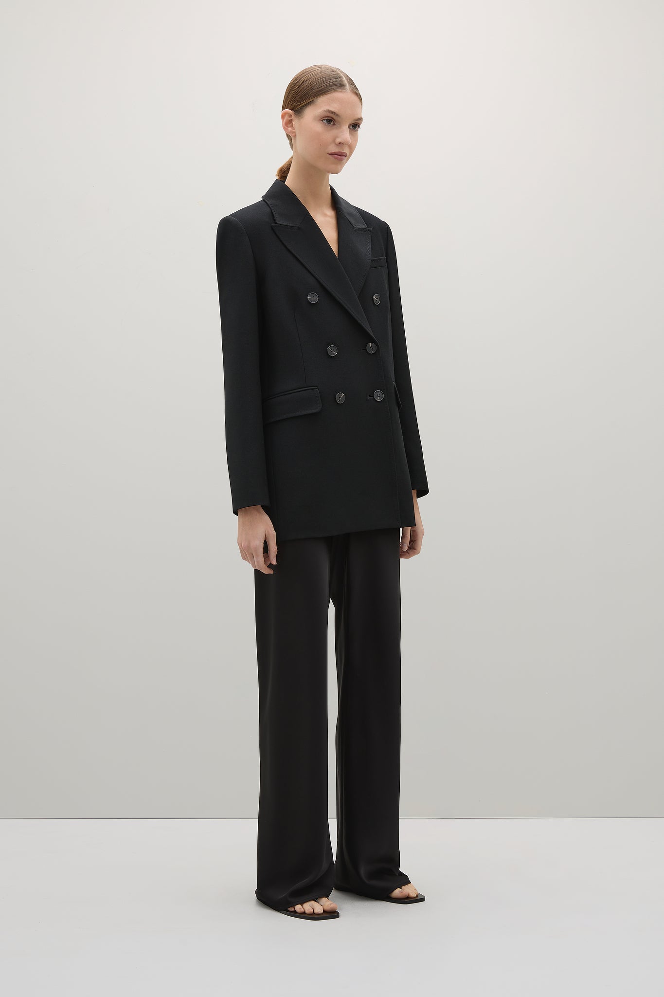 Woman wearing a black suit standing against a plain background