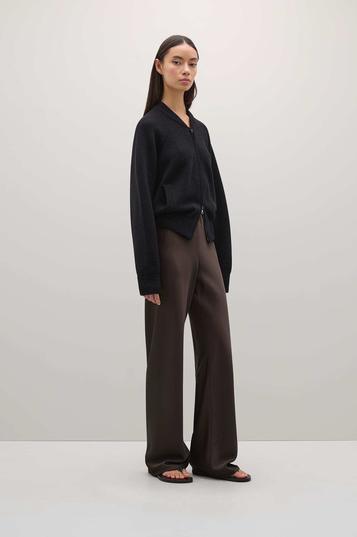 Person wearing a black sweater and brown pants on a white background