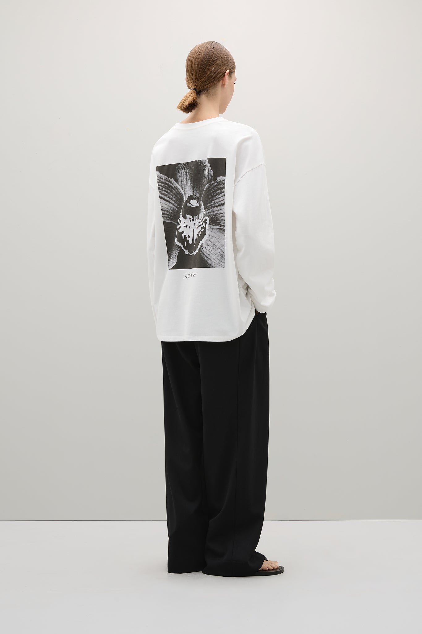 Person wearing a white sweatshirt with a black and white graphic on the back, standing against a plain background.