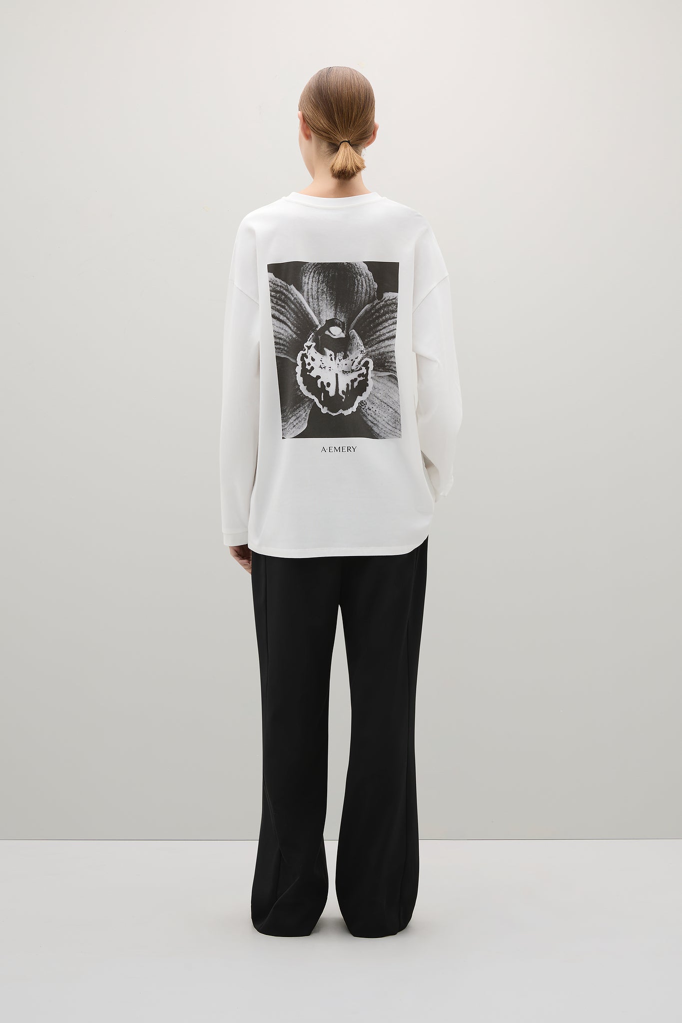 Person wearing a white sweatshirt with a black graphic design on a plain background