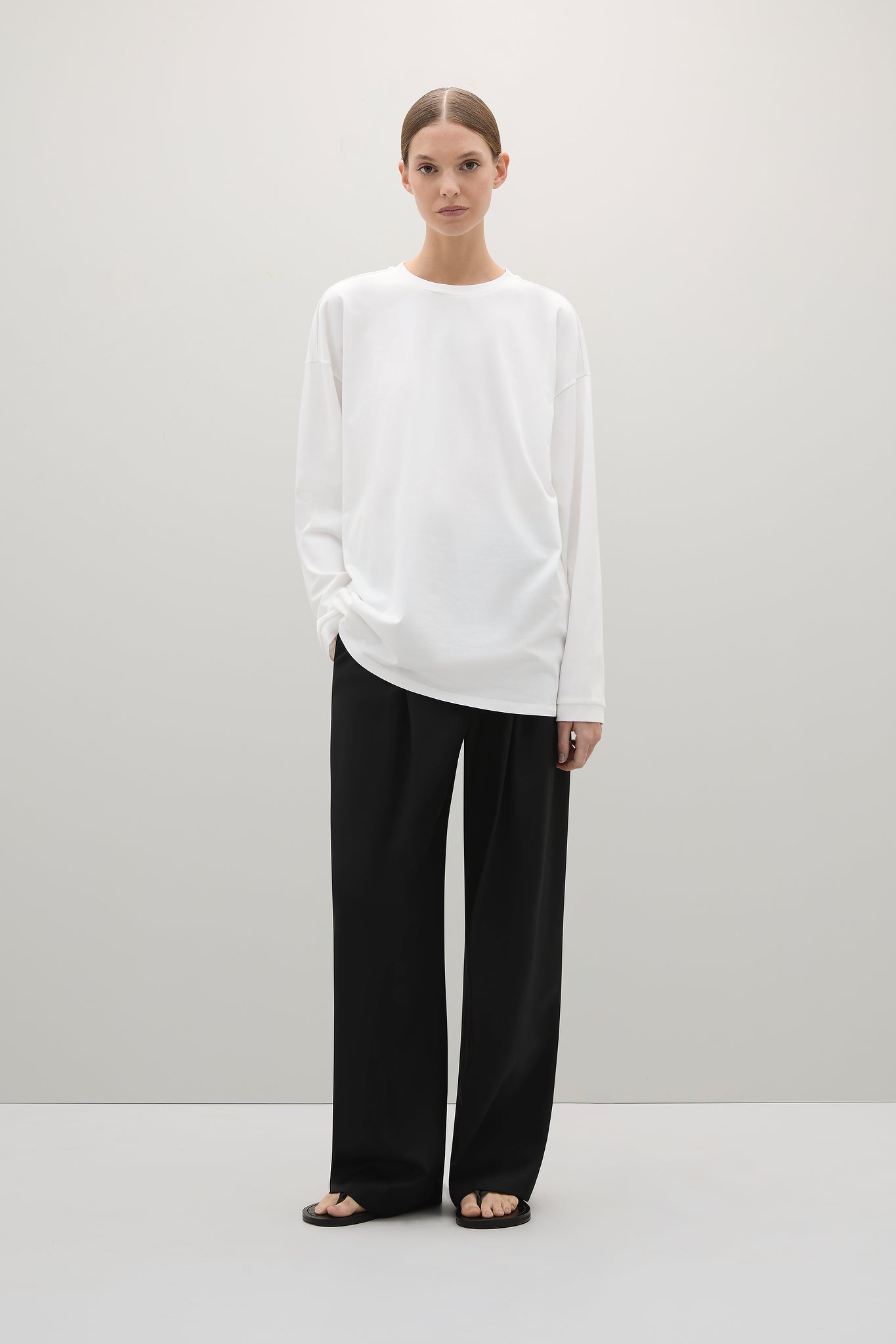 Person wearing a white long-sleeve shirt and black pants on a white background