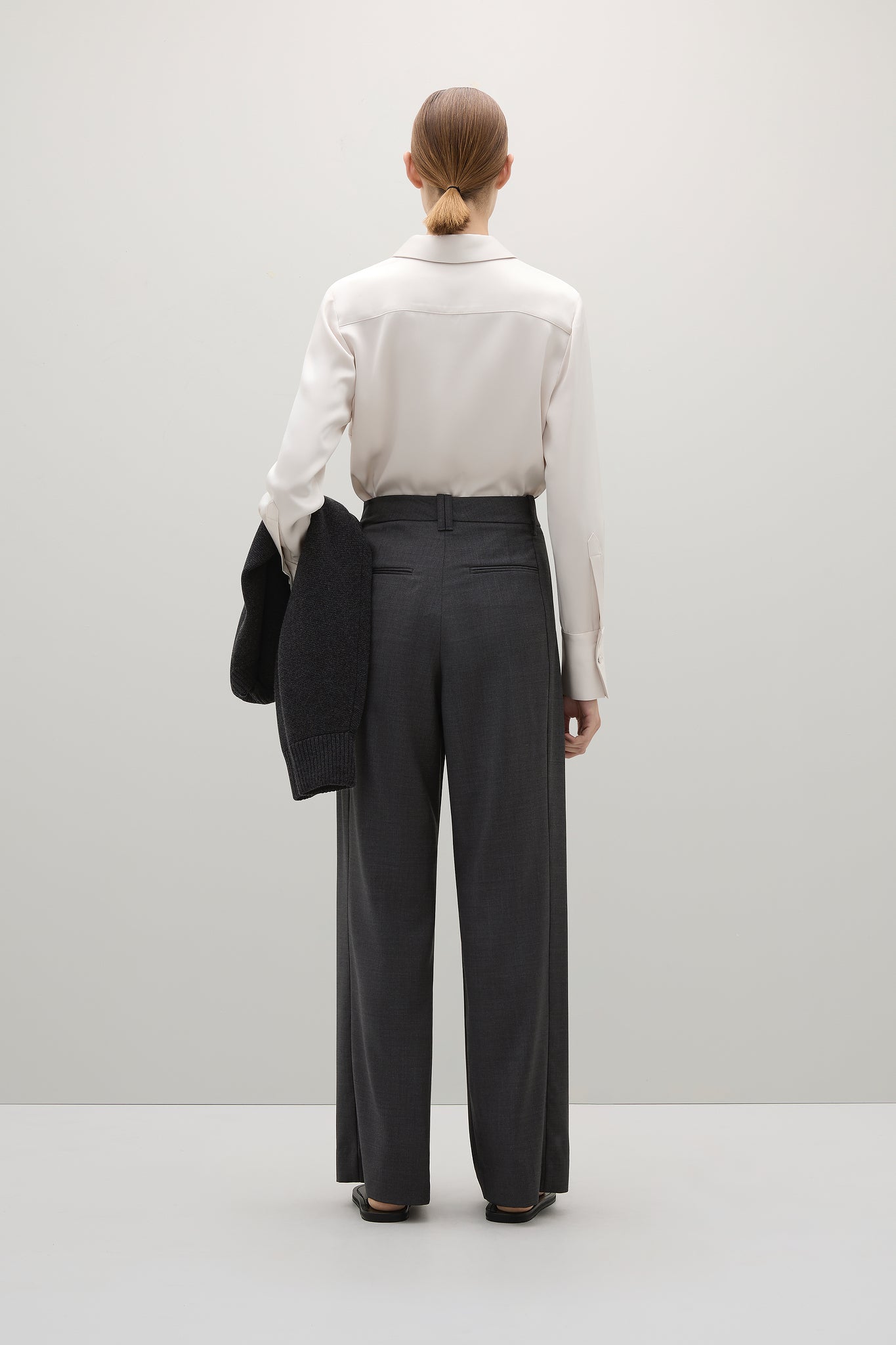 Person wearing a white shirt and dark pants against a plain background