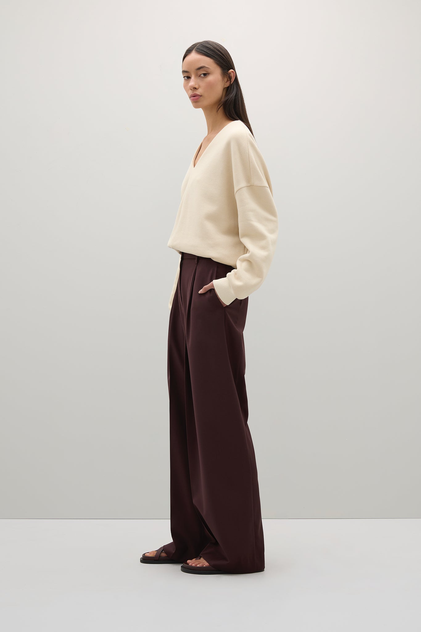 Woman wearing a beige sweater and brown pants on a white background