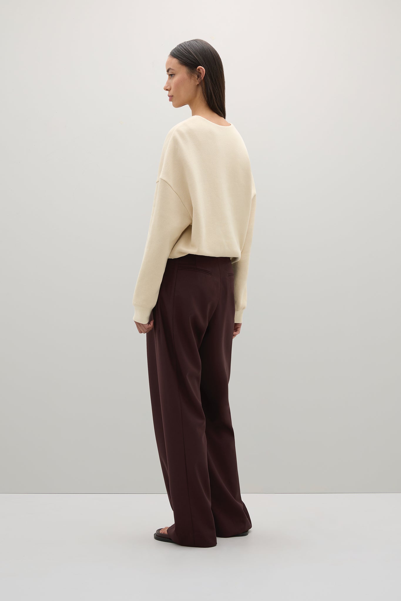 Woman wearing a beige sweater and brown pants on a white background