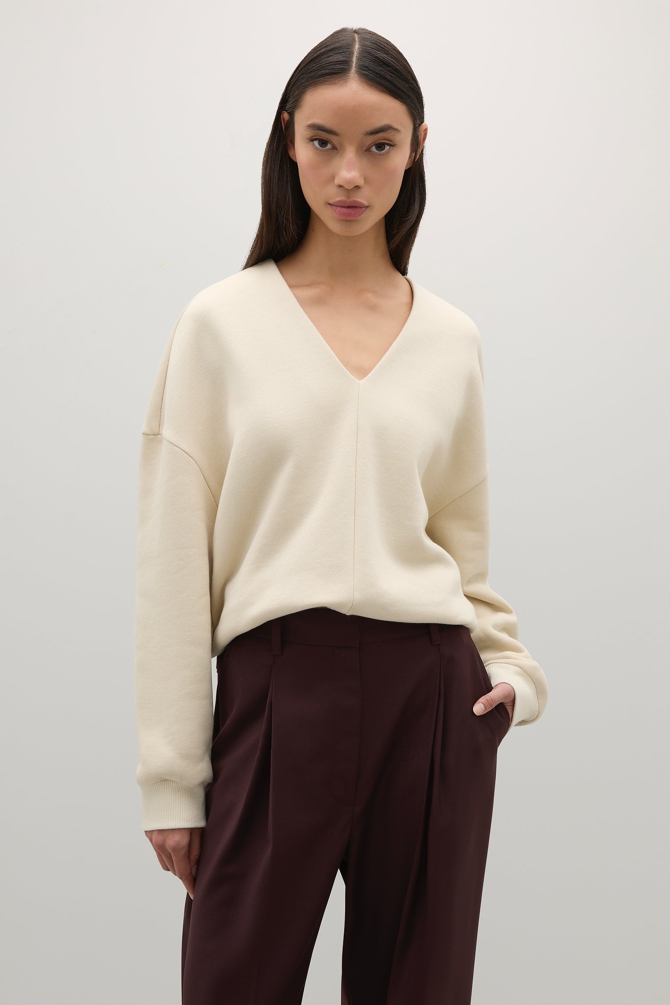 Woman wearing a cream sweater and dark pants against a plain background