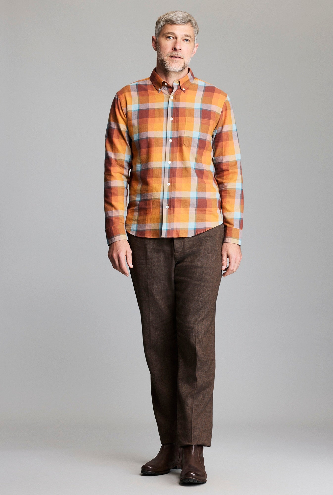 Man wearing a plaid shirt and brown pants against a gray background