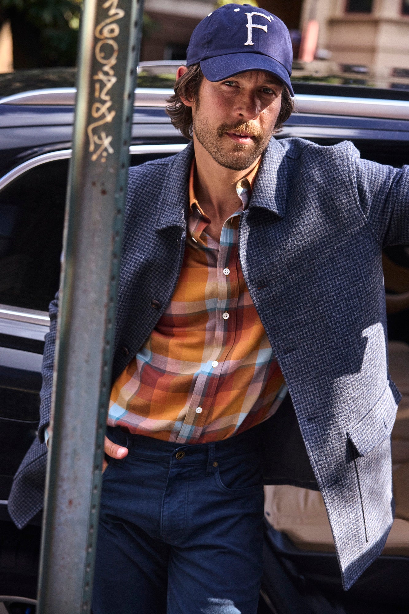 Man wearing a blue cap and checkered shirt, standing next to a car.