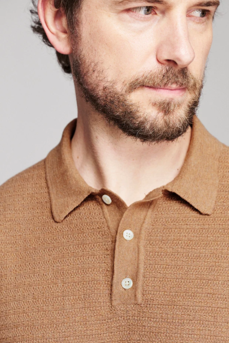 Close-up of a man wearing a textured knit polo shirt in a warm camel brown color, featuring a classic collar and three buttons.
