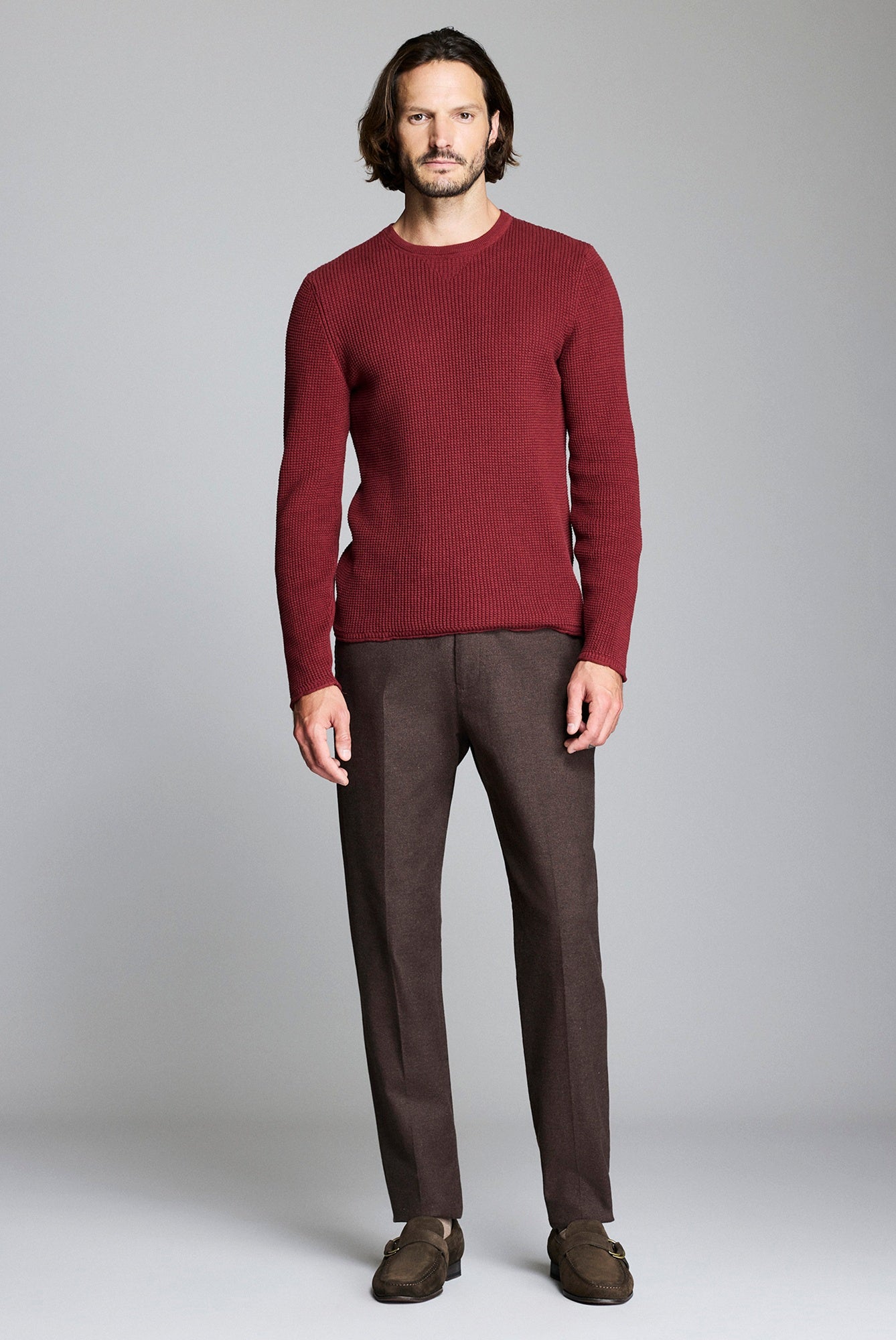 Man wearing a burgundy sweater and brown pants against a plain background