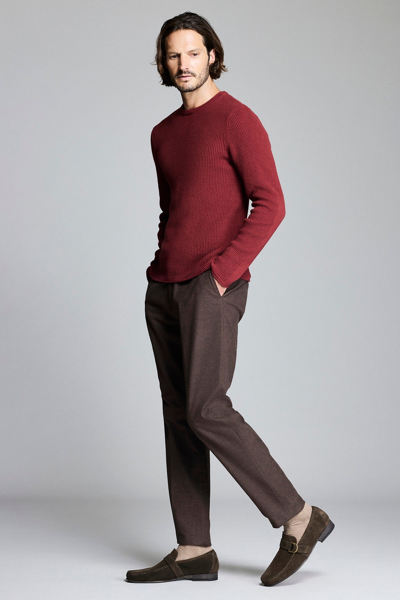Man wearing a burgundy sweater and brown pants on a plain background