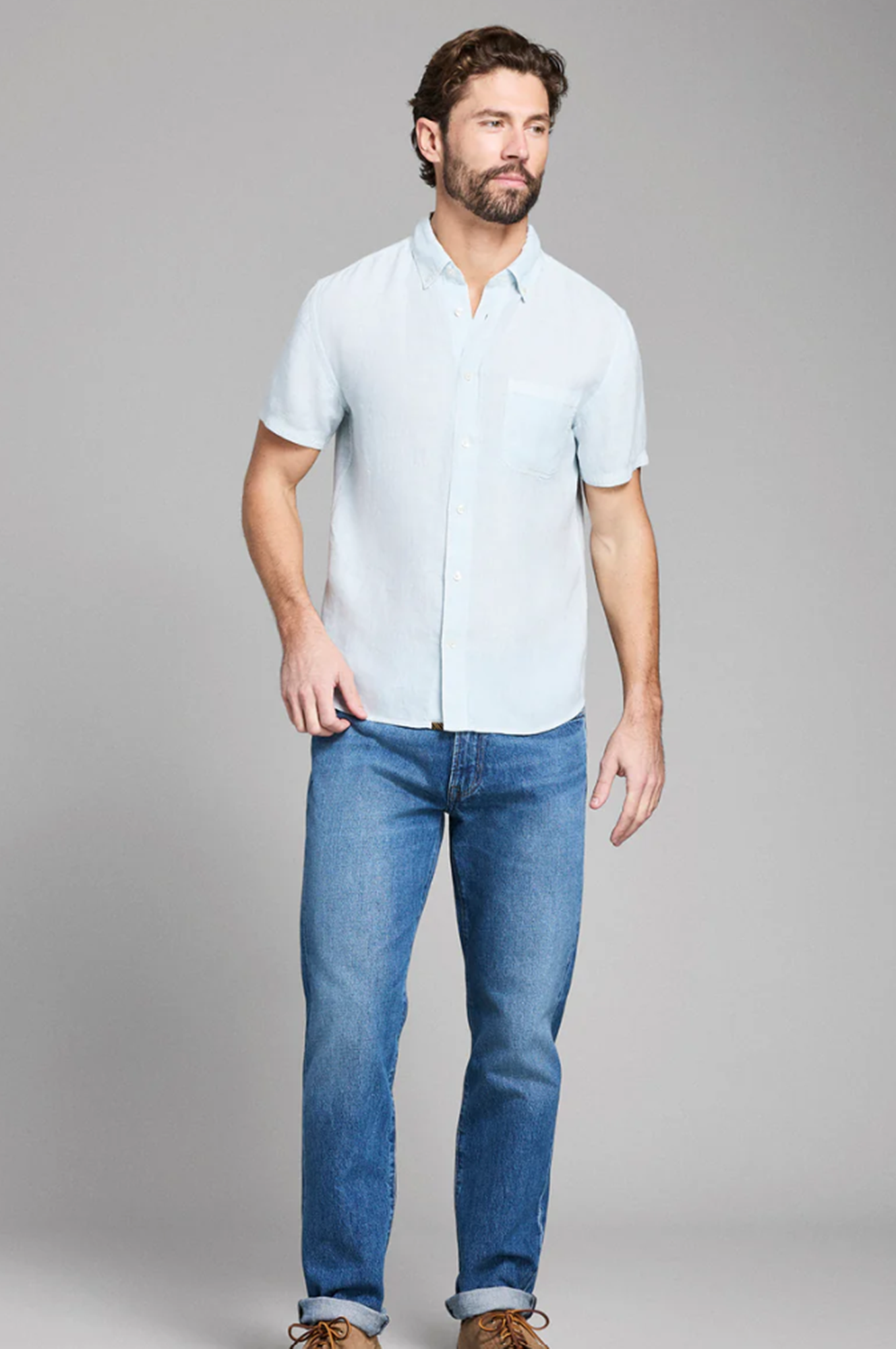 Man wearing a light blue shirt and jeans on a gray background