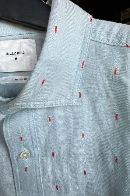 Light blue shirt with red pattern and visible brand label on a dark background