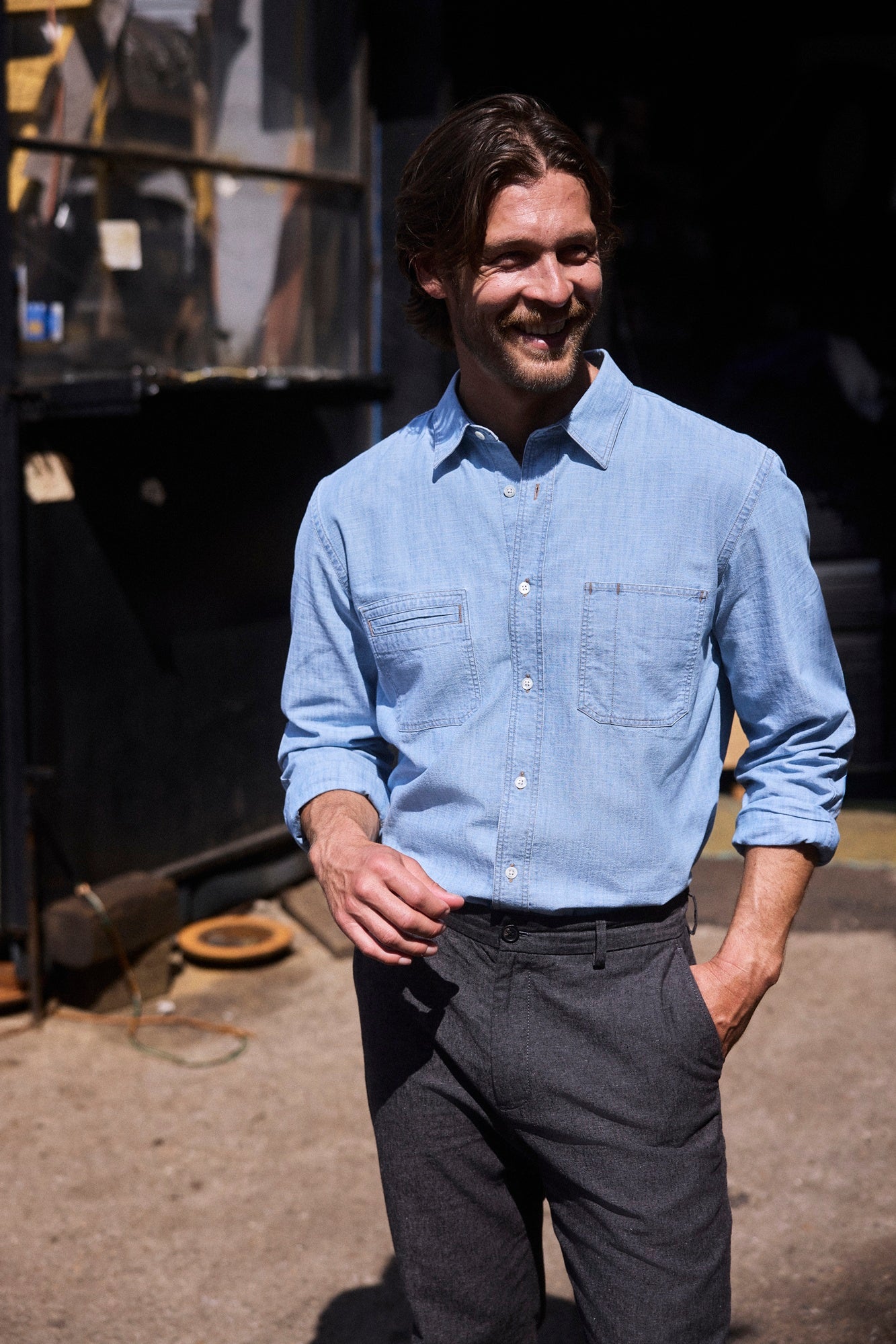 Man wearing a light blue shirt and dark gray pants standing outdoors.