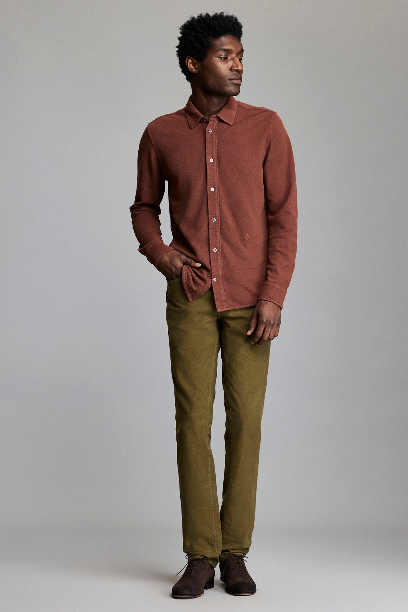 Man wearing a brown shirt and green pants against a plain background