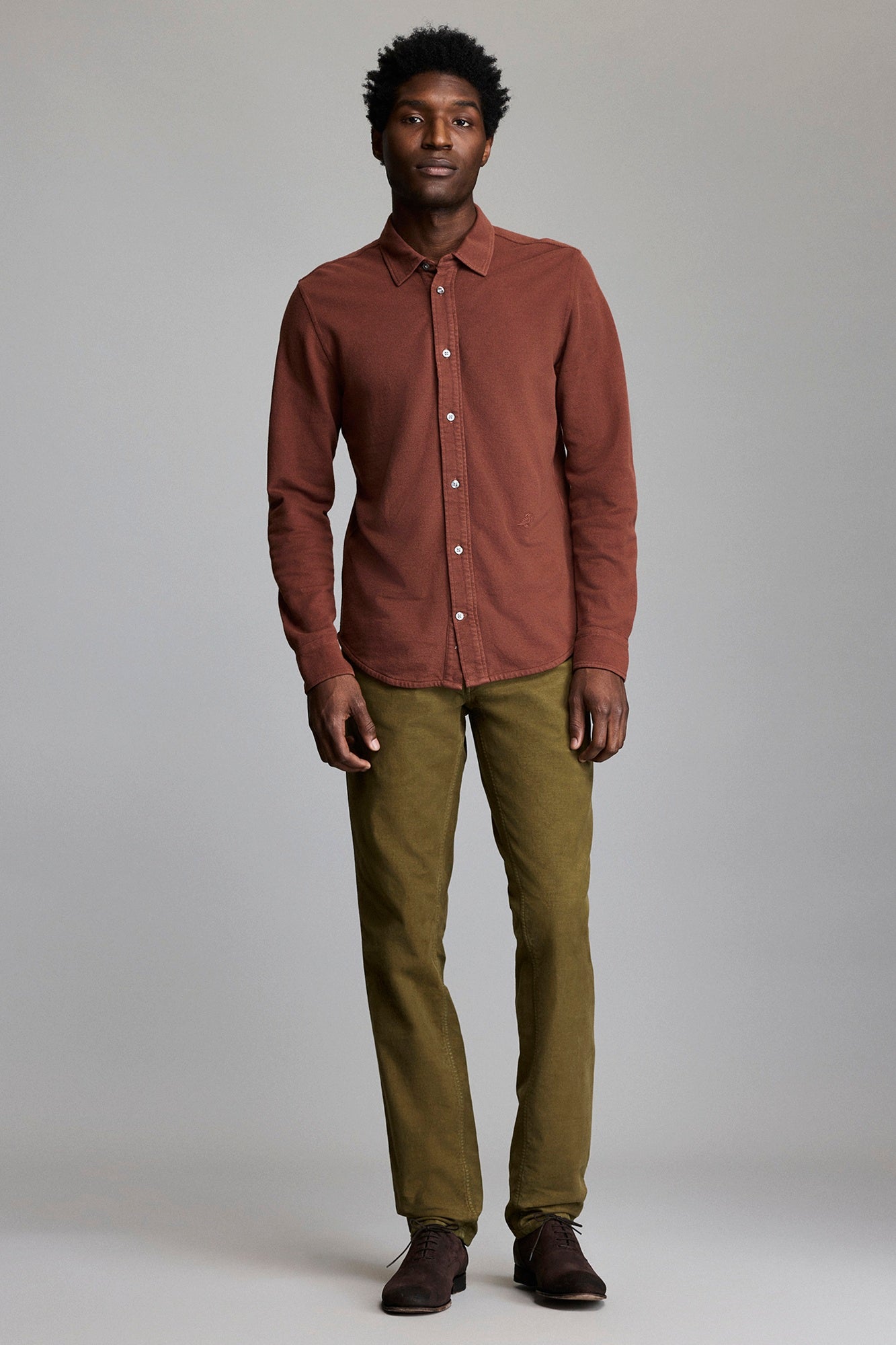 Man wearing a brown shirt and green pants against a plain background