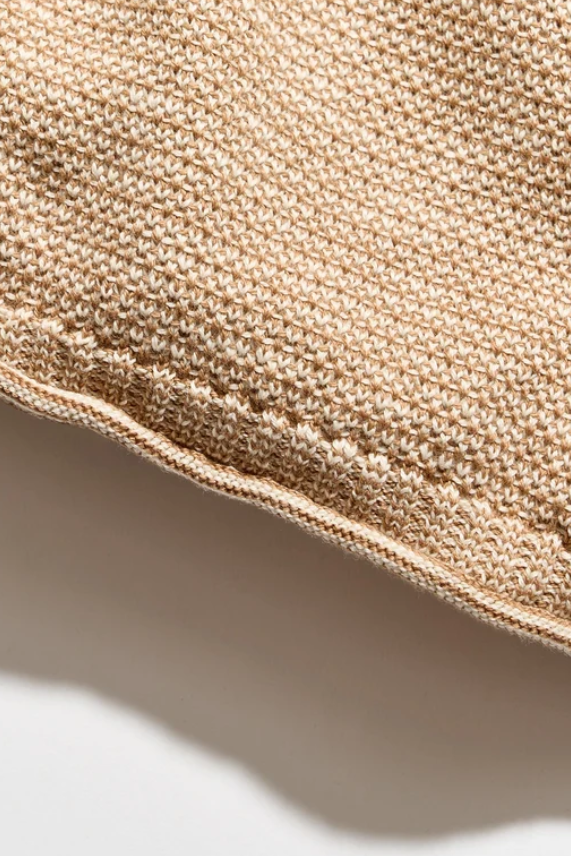 Close-up of a beige knitted textile with a ribbed edge, shown against a white background with a soft shadow.