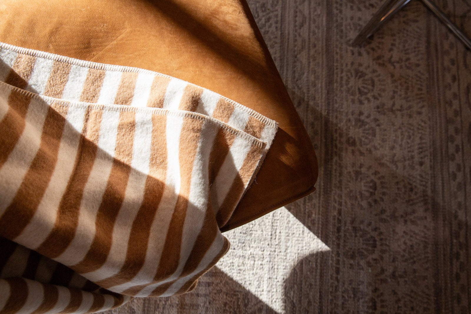 Brown and cream striped throw blanket draped over a leather chair, part of the Home Decor collection at Maison Avenir in Greenville, SC.