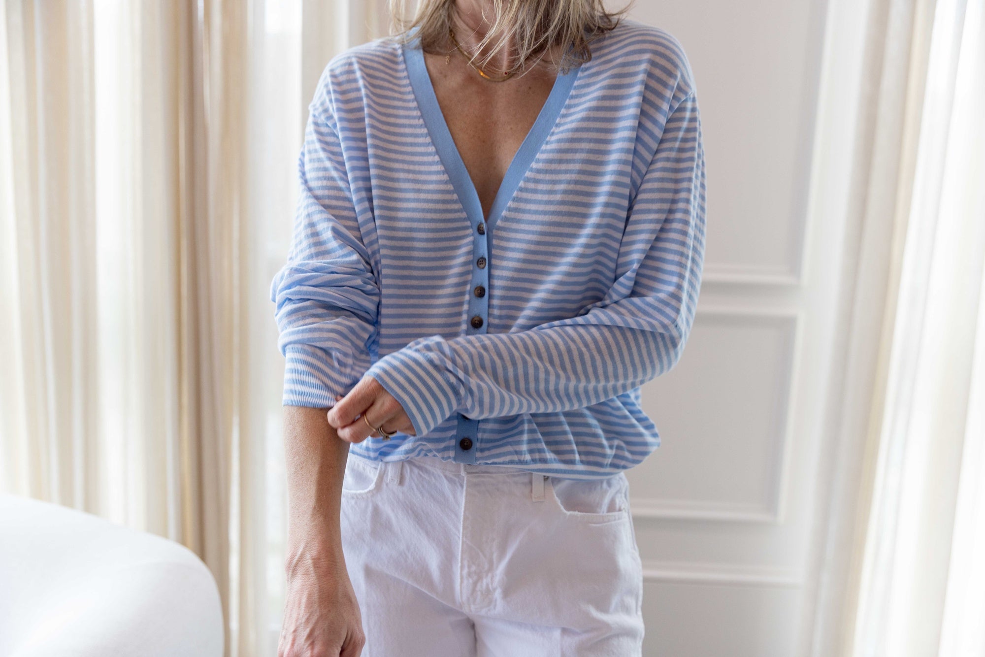 Close up of a woman wearing the ciao lucia jorgie cardigan standing in a room with white curtains.