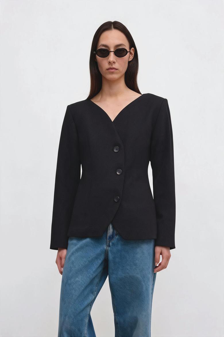 A model wearing a black wrap-style blazer with three front buttons and a V-neckline, paired with blue jeans and black sunglasses, against a plain light gray background.