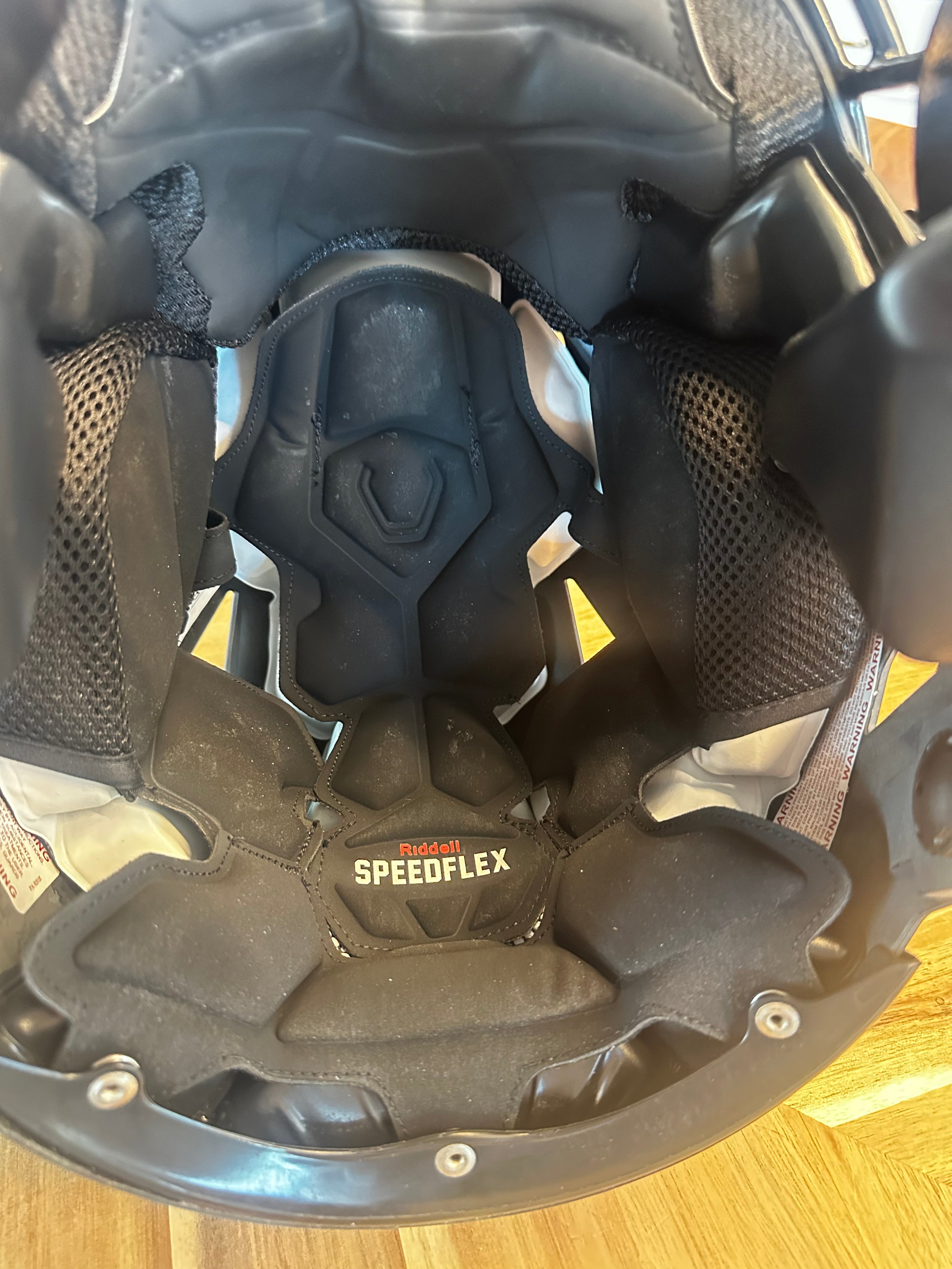Close-up of the inside of a black protective helmet showing the Speedflex neck guard and interior padding, photographed on a wooden floor.