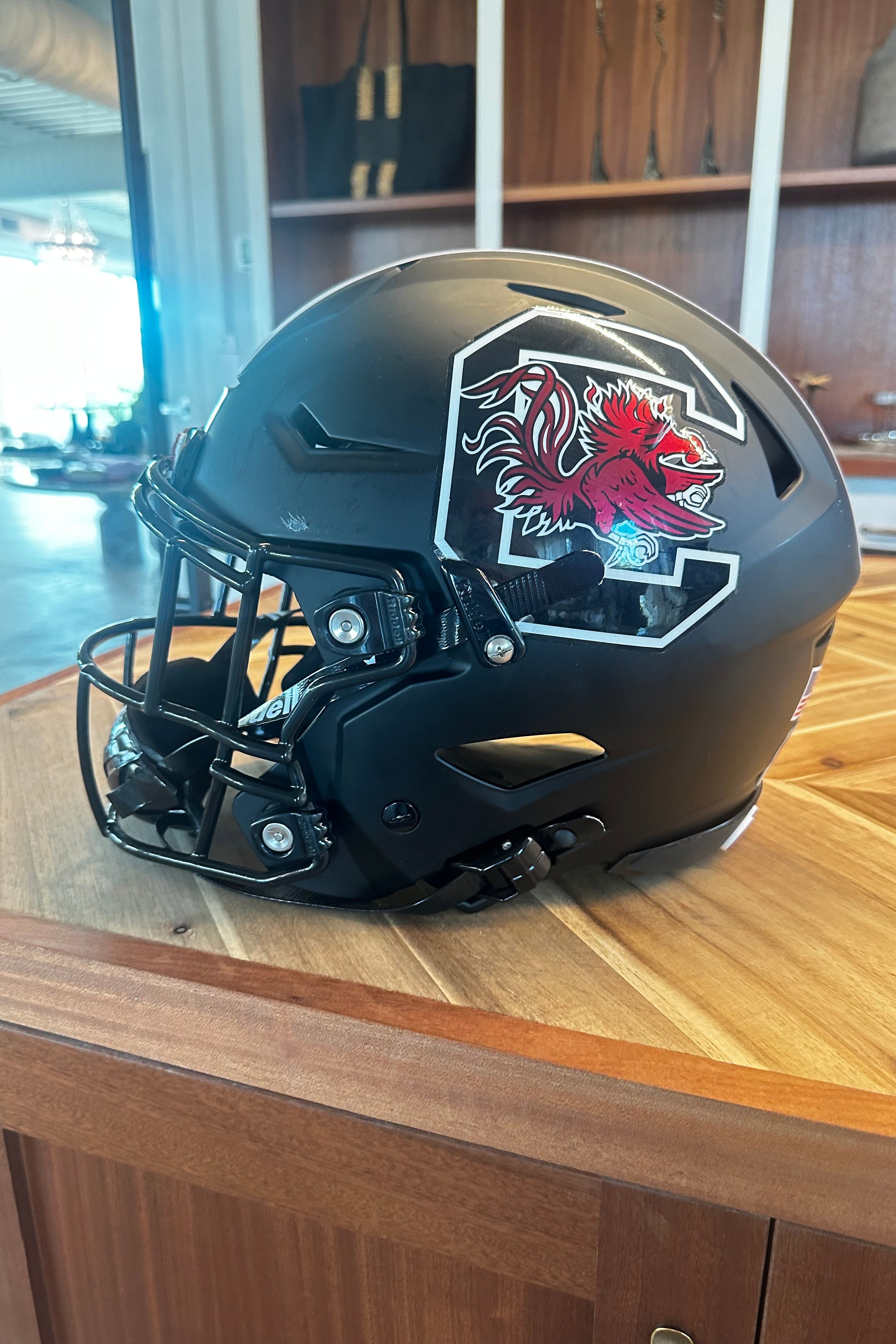 A matte black South Carolina Gamecocks football helmet with a red and white logo decal, resting on a wooden table in an indoor setting.