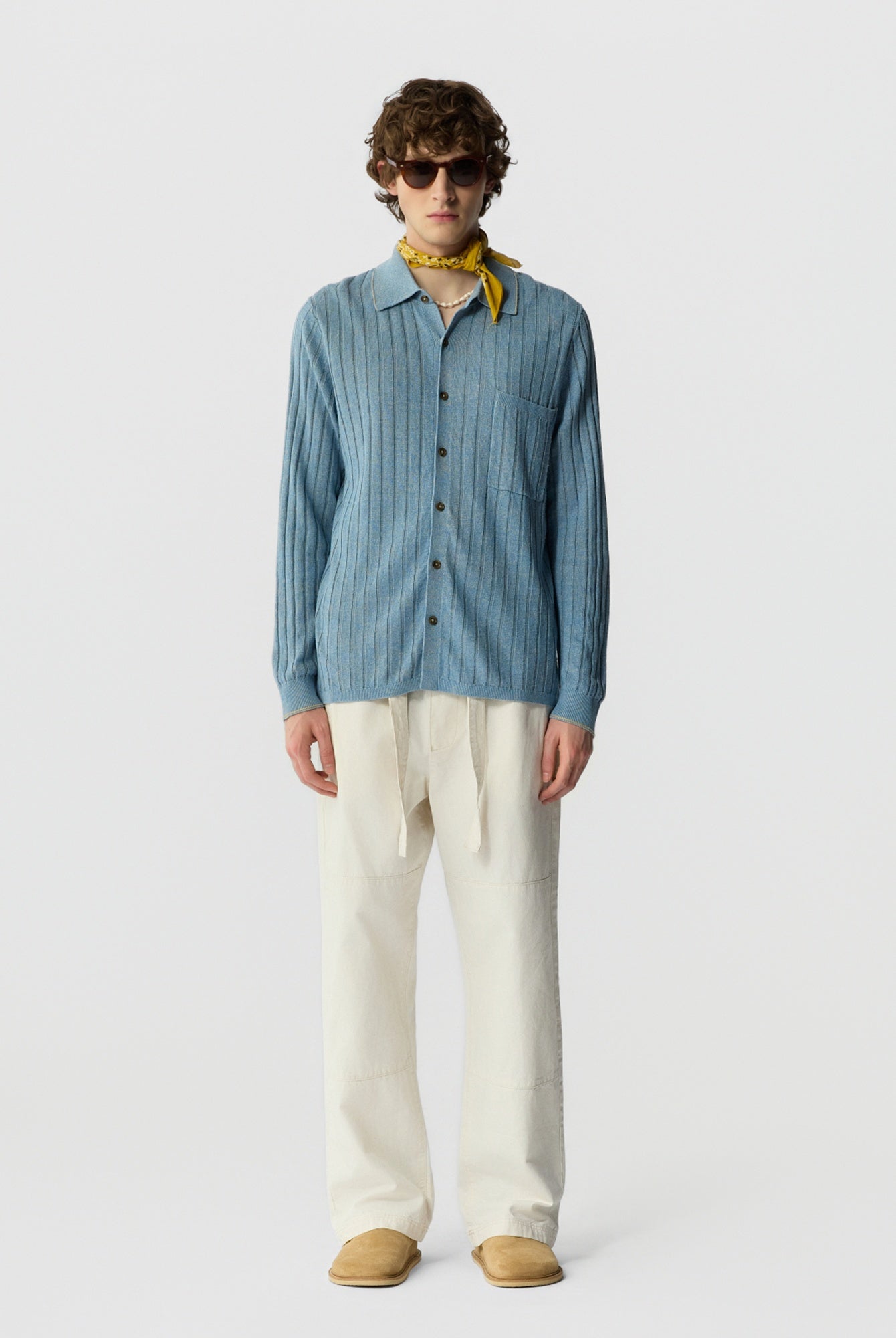 Man wearing a blue striped shirt, beige pants, and sunglasses on a white background