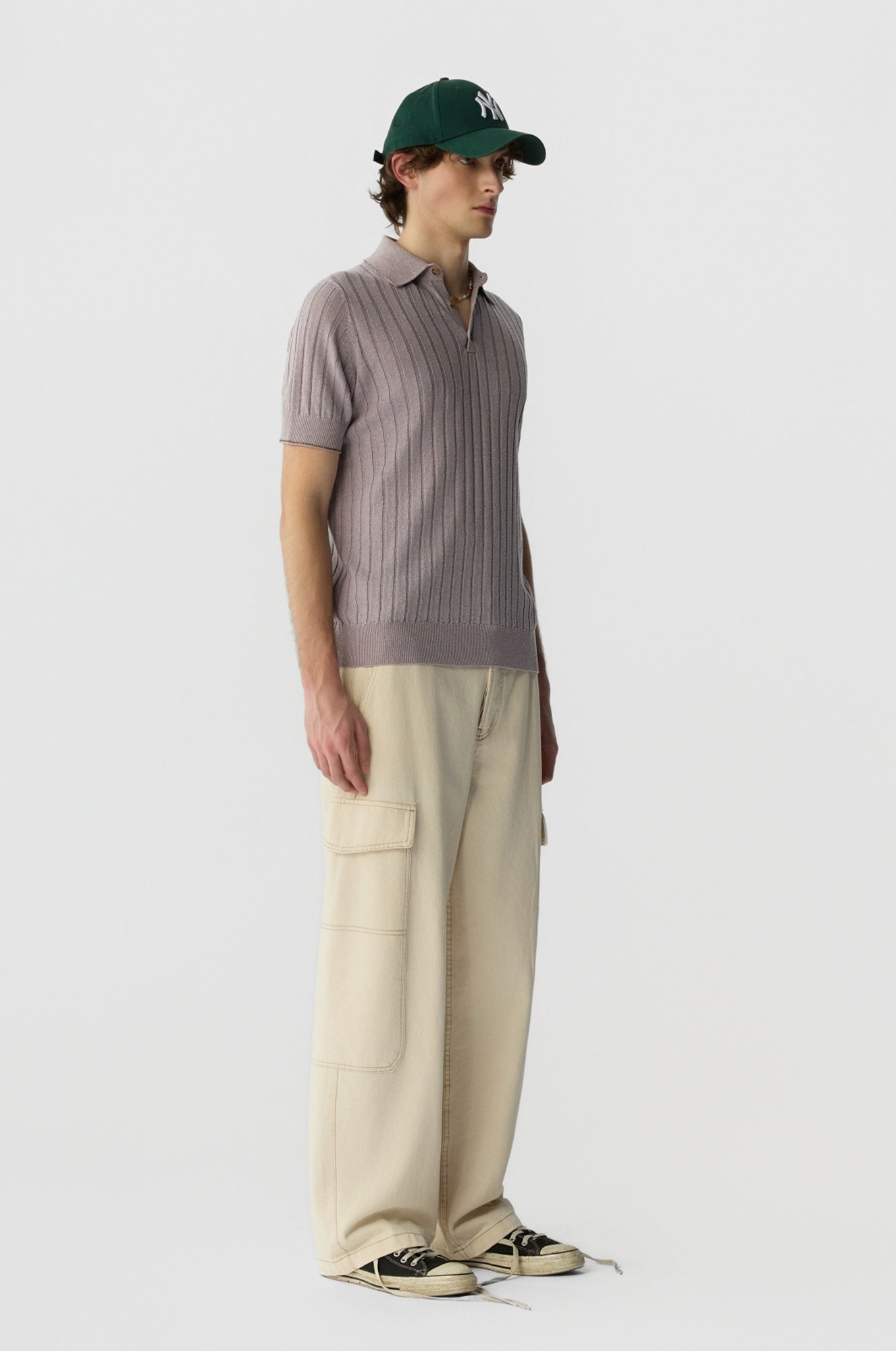 Person wearing a brown ribbed shirt, beige cargo pants, and a green cap on a white background