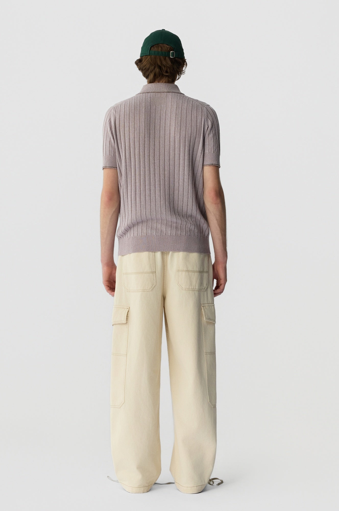 Person wearing a ribbed knit sweater and beige pants on a white background