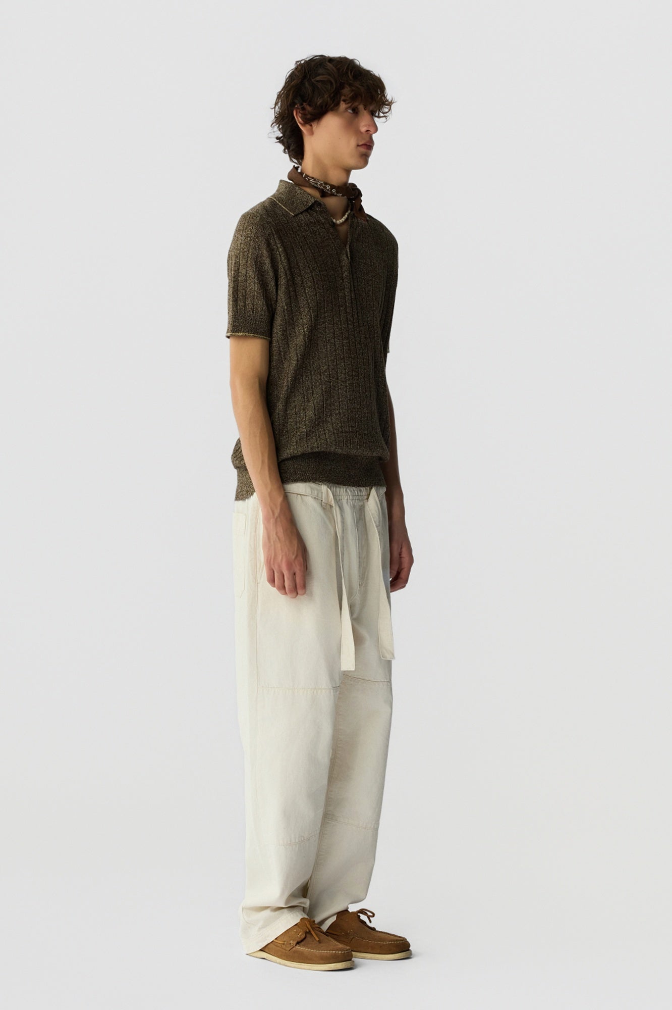 Man wearing a brown polo shirt and beige pants on a white background