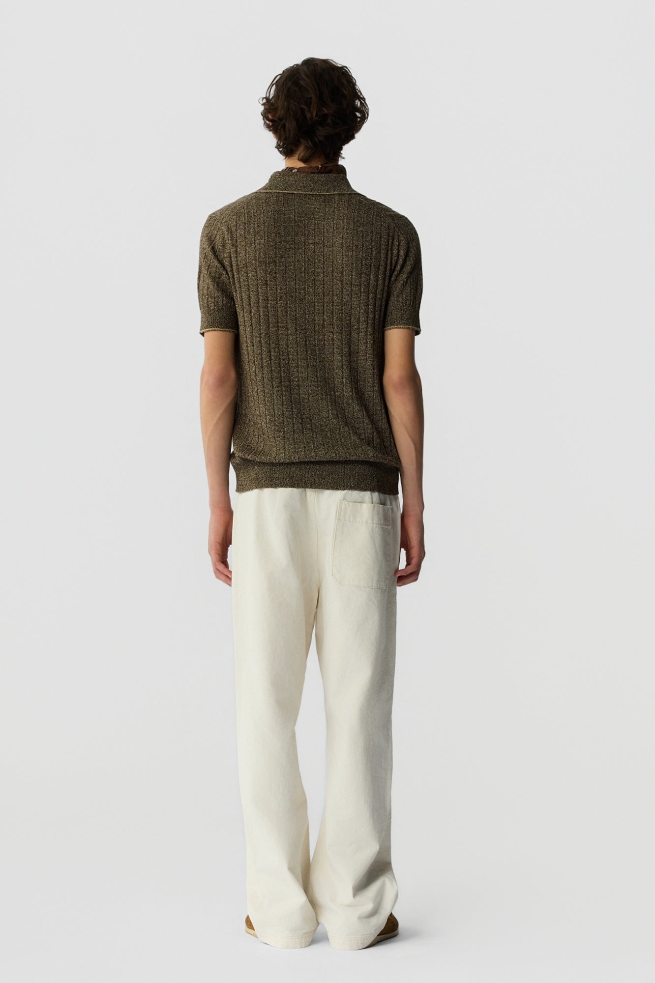 Person wearing a green textured polo shirt and white pants on a light gray background