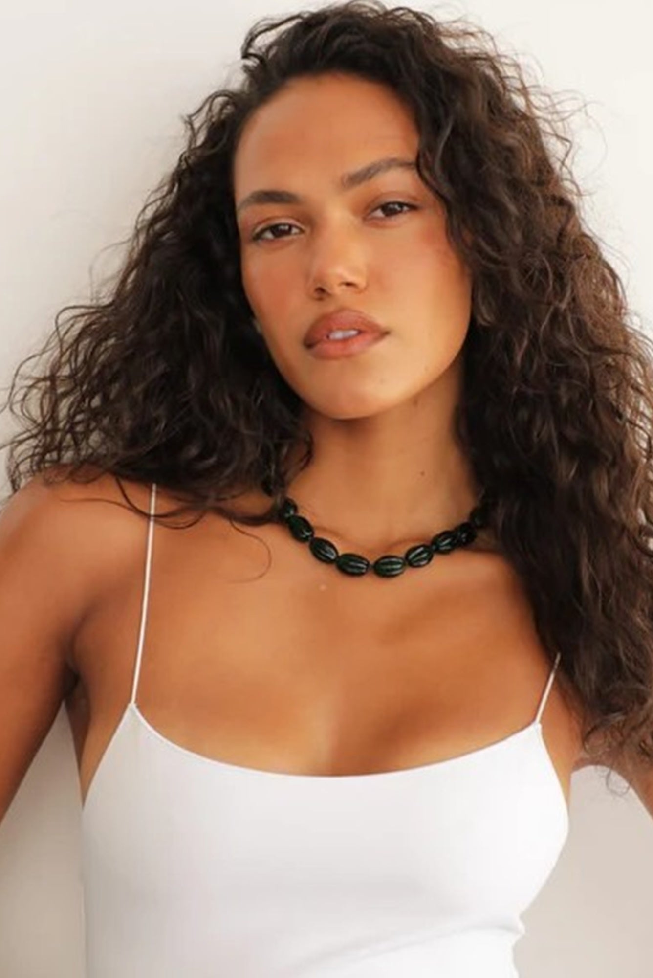 Woman wearing a white top and black necklace against a plain background