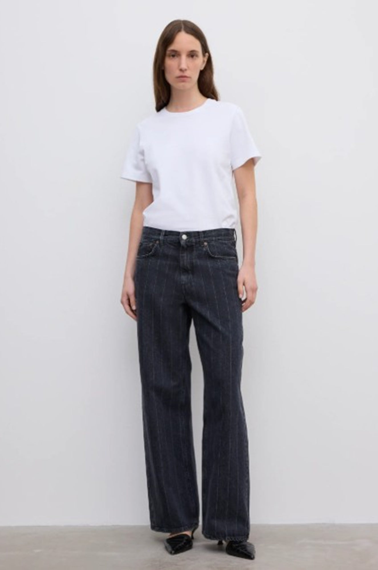 Person wearing a white t-shirt and dark jeans on a plain background