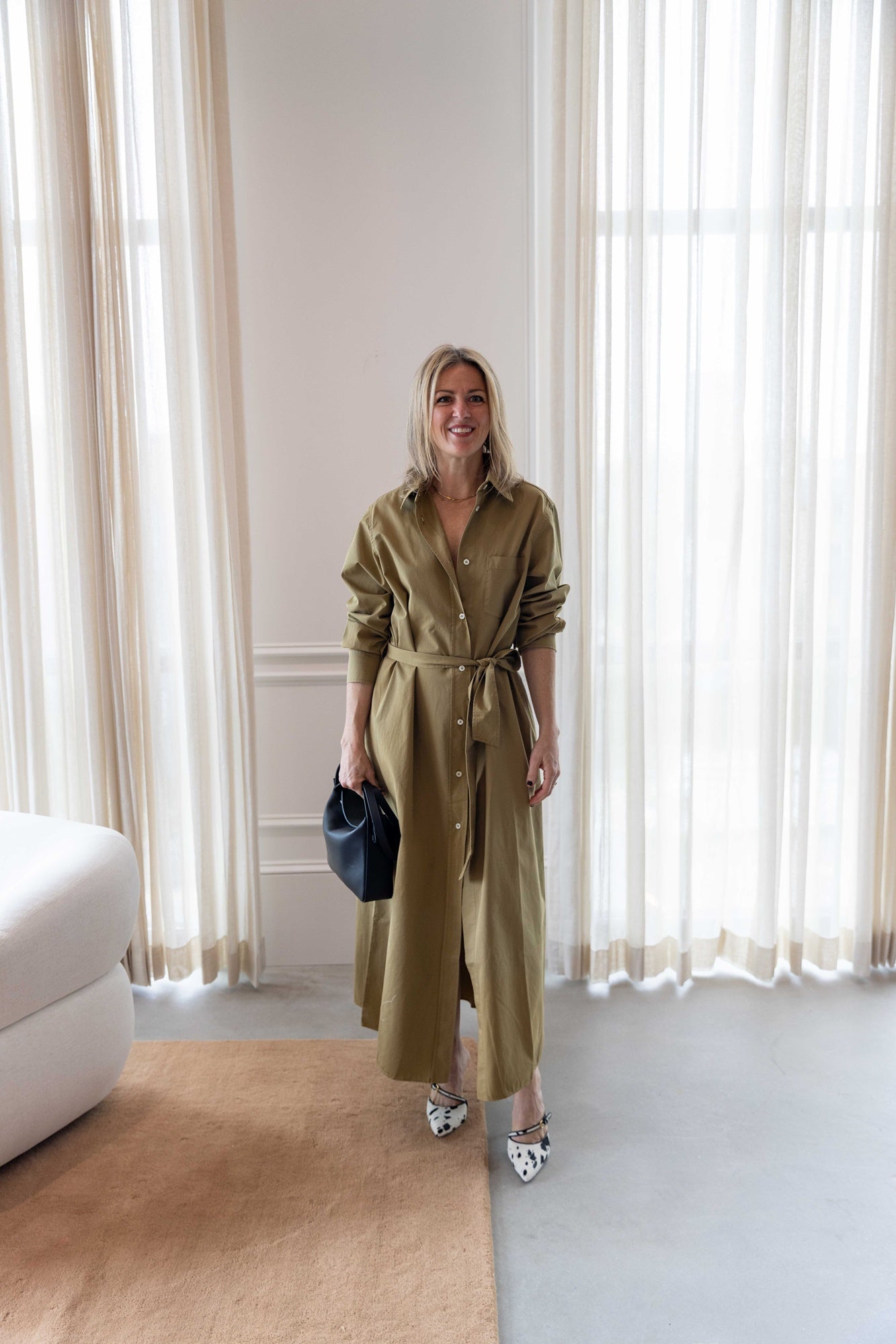 Woman wearing the green house of dagmar belted shirt dress standing in a room with white curtains.