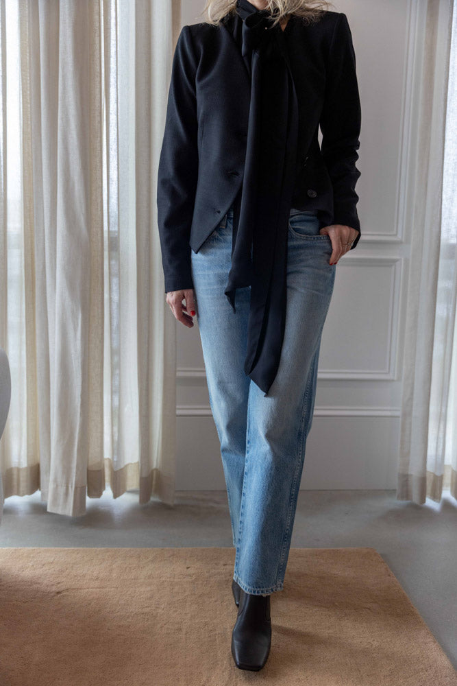 Dagmar Chiffon Scarf Blouse in black viscose, full length under a black jacket with light-wash denim and black boots