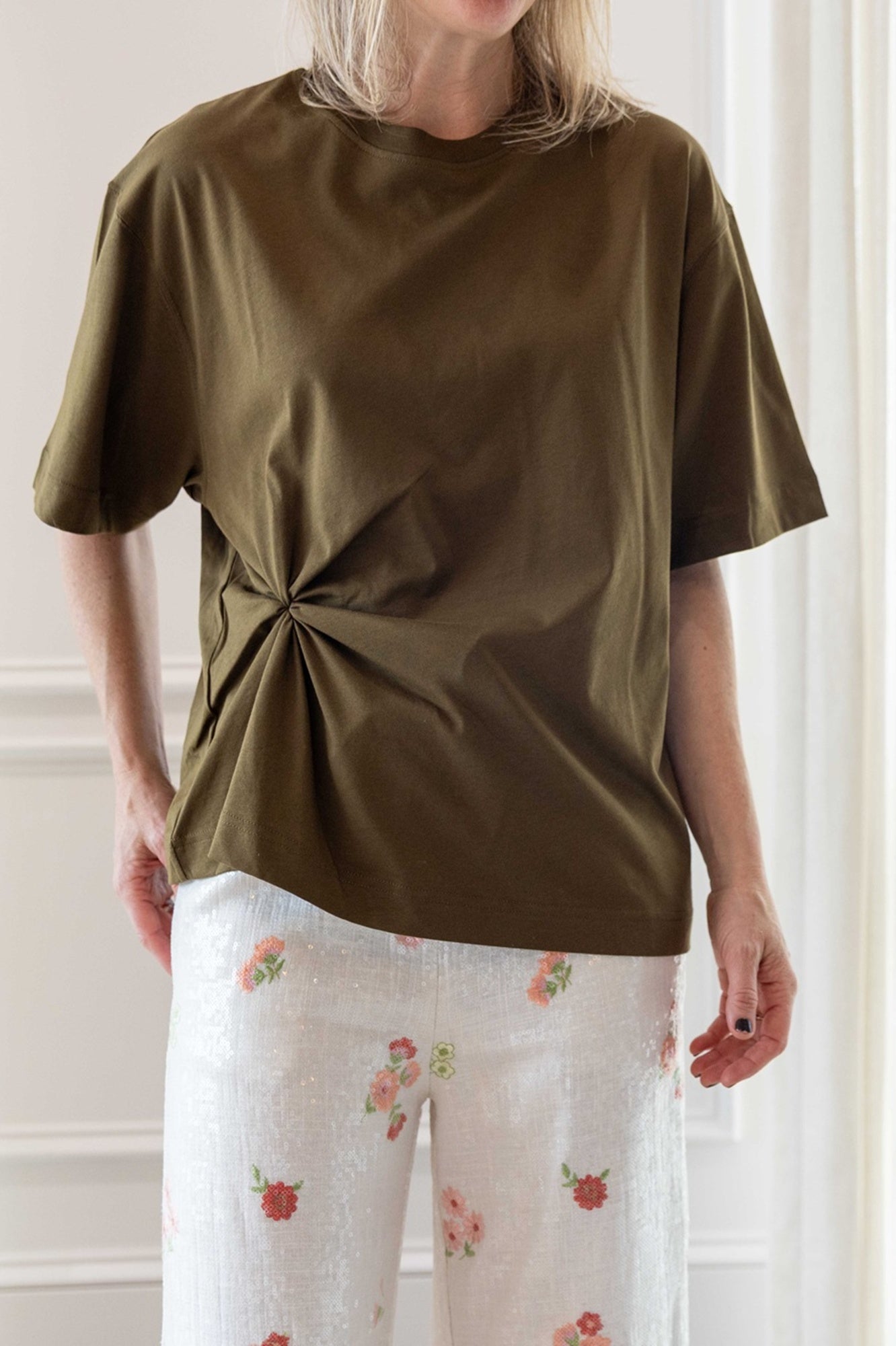 Close up of a woman wearing the house of dagmar knot t-shirt in green and the alfie grace sequin pant in floral.
